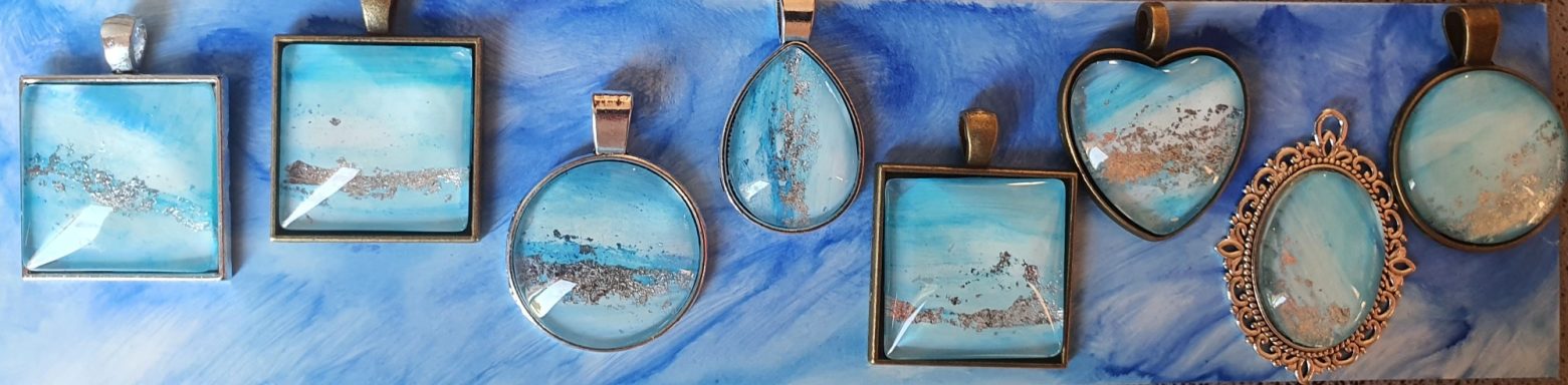 Collection of square, round, teardrop and oval pendants containing original light blue & silver artwork resting on background of darker blue