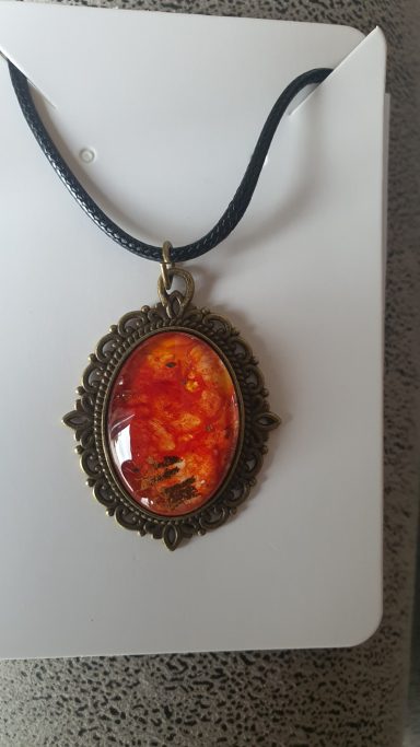 Oval bronzed pendant containing firery red and orange original art work