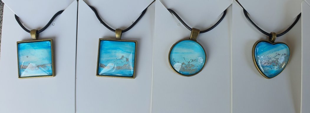 Two square, one round and one heart bronzed pendants containing light blue and silver original art work