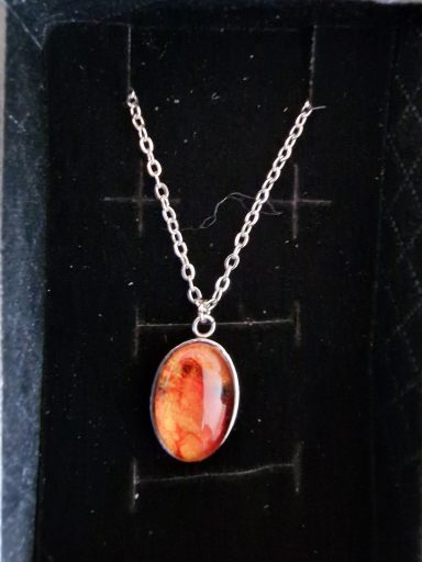 Stainless steel oval pendant containing parts of original art orange, red, gold and black.