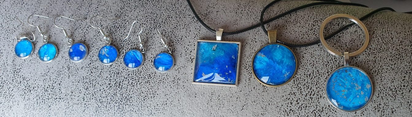 Stainless steel earrings, pendants and keyrings all containing deep blue and silver gilded original art work