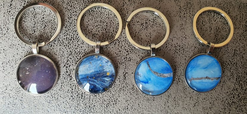 Two silver keyrings containing original art work. Left is dark blue & gold from "Midnight seas". Right is sky blue & silver "Open Skes"