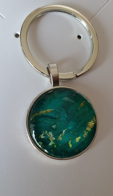 Silver round keyring containing dark green and gold gilded original art work