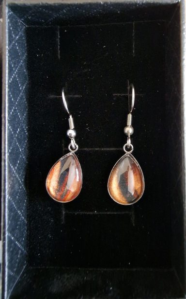 Stainless steel tear drop earrings containing parts of original art orange and black with gold shimmer on a black background.